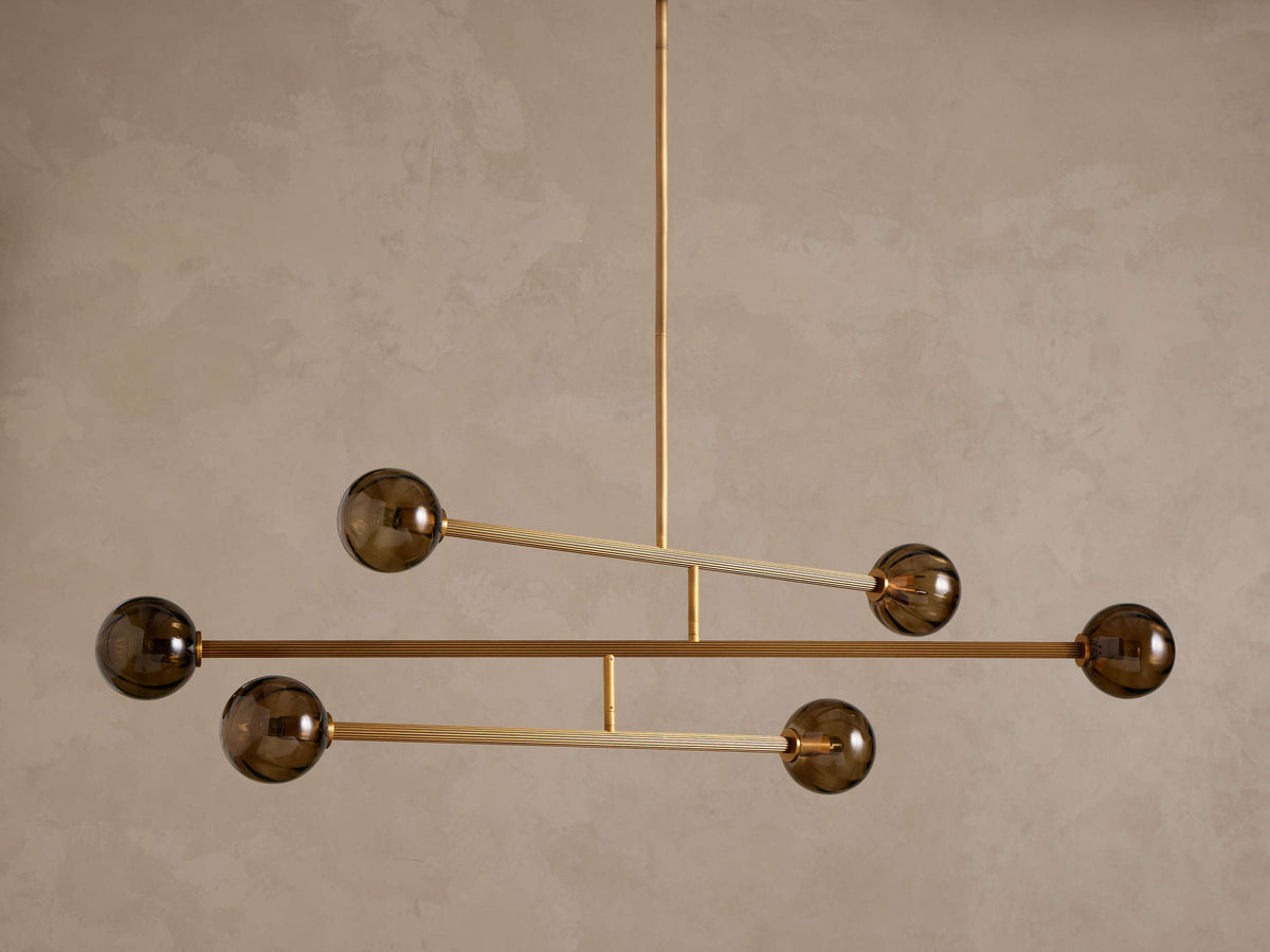 Modern chandelier with a brass frame and five smoky brown glass globe shades, suspended from above.