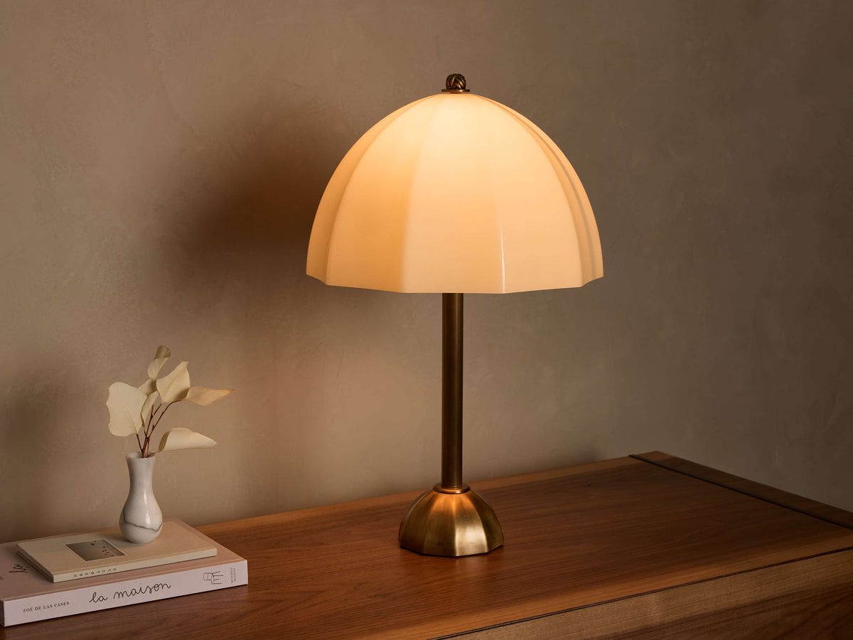 Front view of a cream ribbed glass table lamp with a brass stem and base, casting a warm glow on a wooden surface.