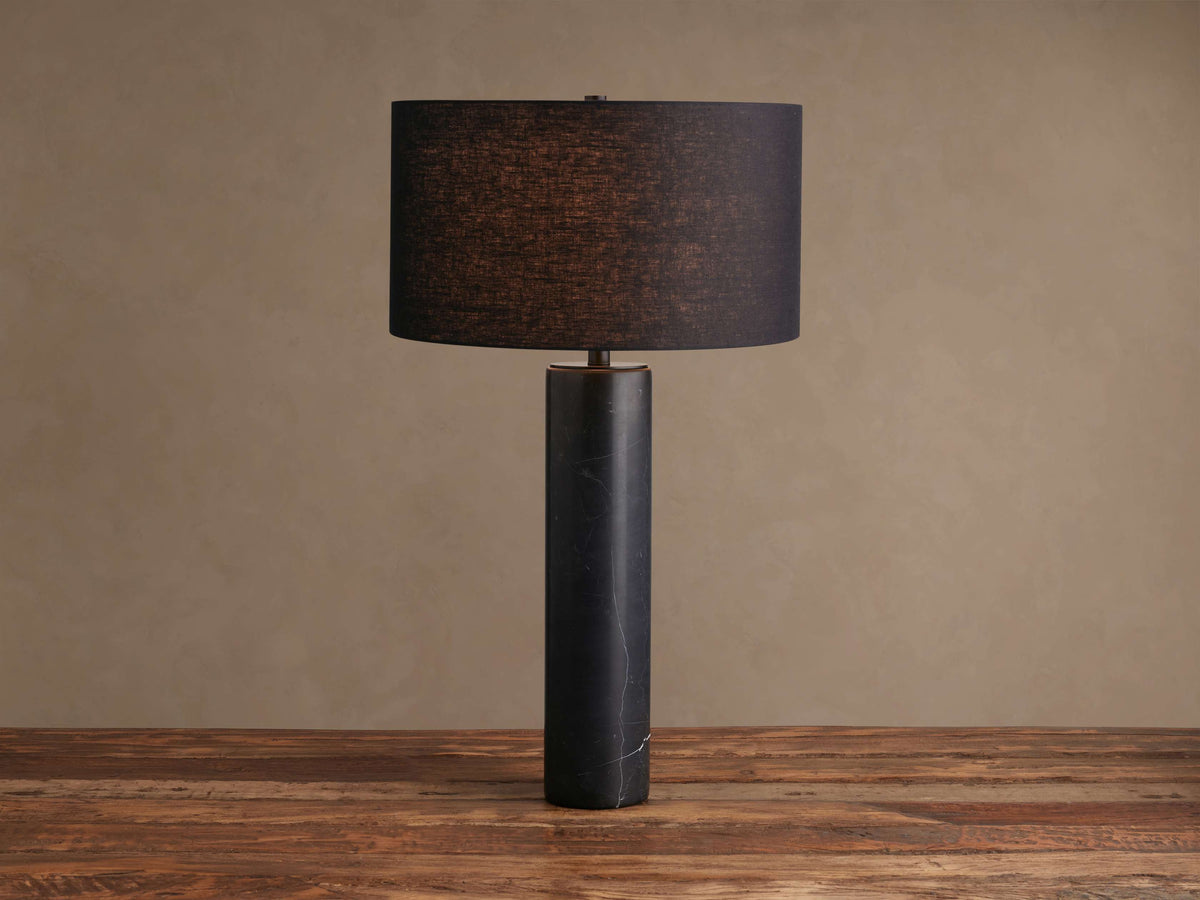 Brixton Table Lamp with a black marble column, brass accent, and dark fabric drum shade on a rustic wood table.