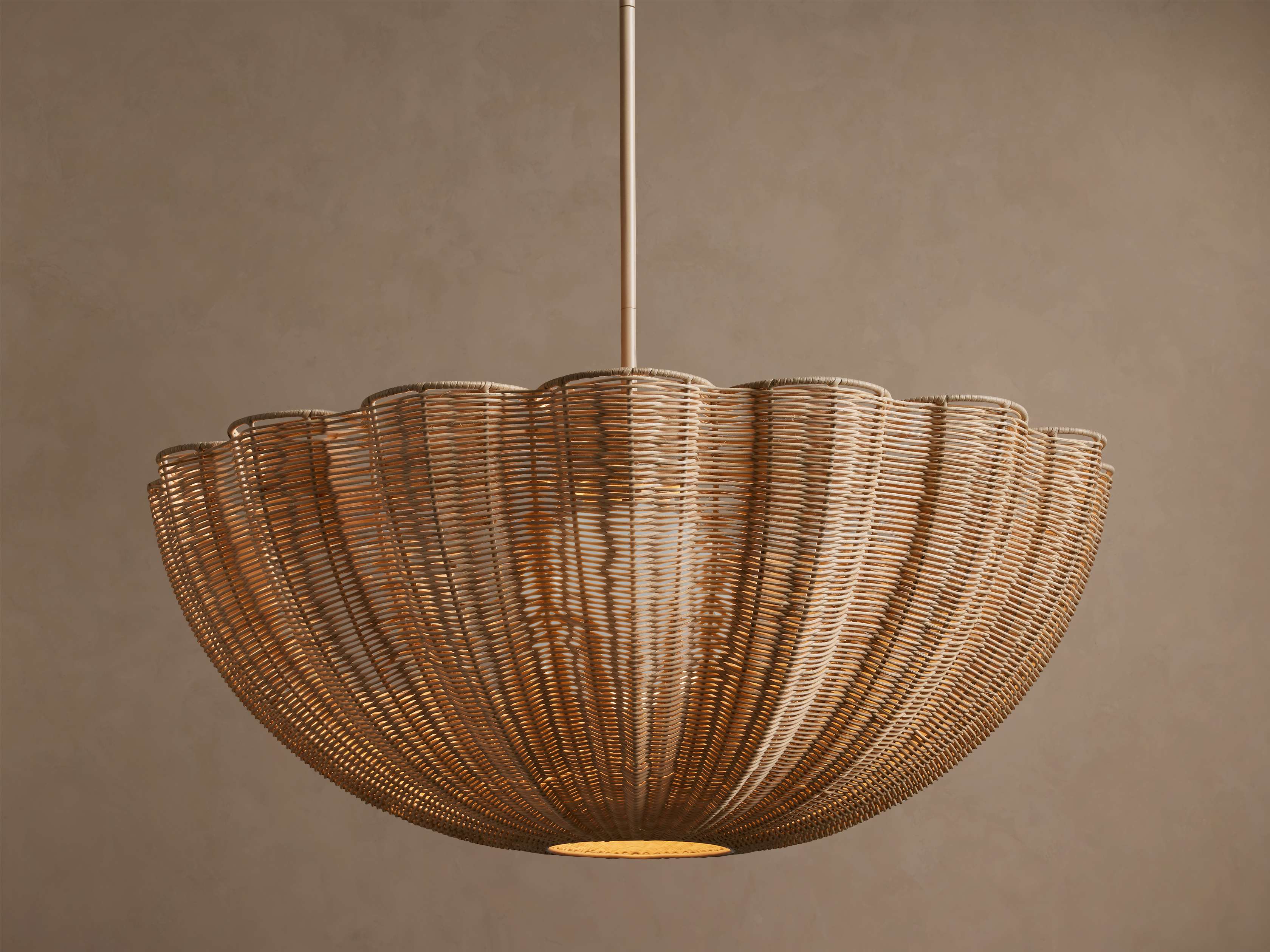 Claire Pendant: Light brown woven rattan pendant light, wide scalloped shell shape, hanging from a pole, glowing.