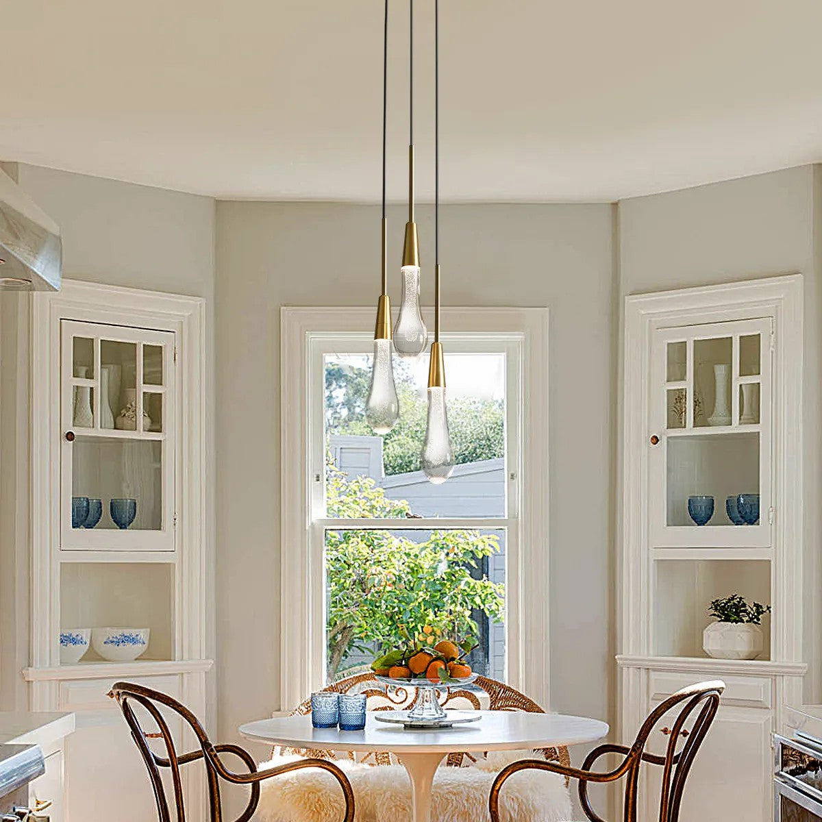 A pendant light with black PVC cords and brass-finished integrated LED lights, hanging over a dining table in a room with light-colored walls.