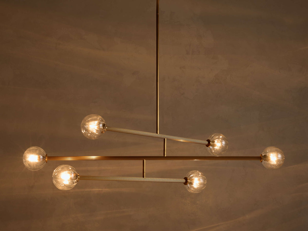 Front view of modern chandelier with illuminated clear glass ribbed globes and brass-toned metal arms.