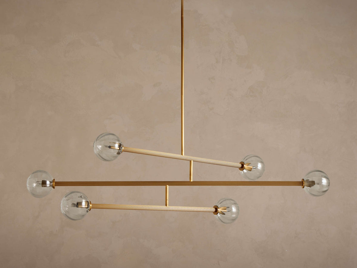 Front view of a modern Linear Gold and Glass Chandelier with five clear glass globes and reeded gold-colored rods.