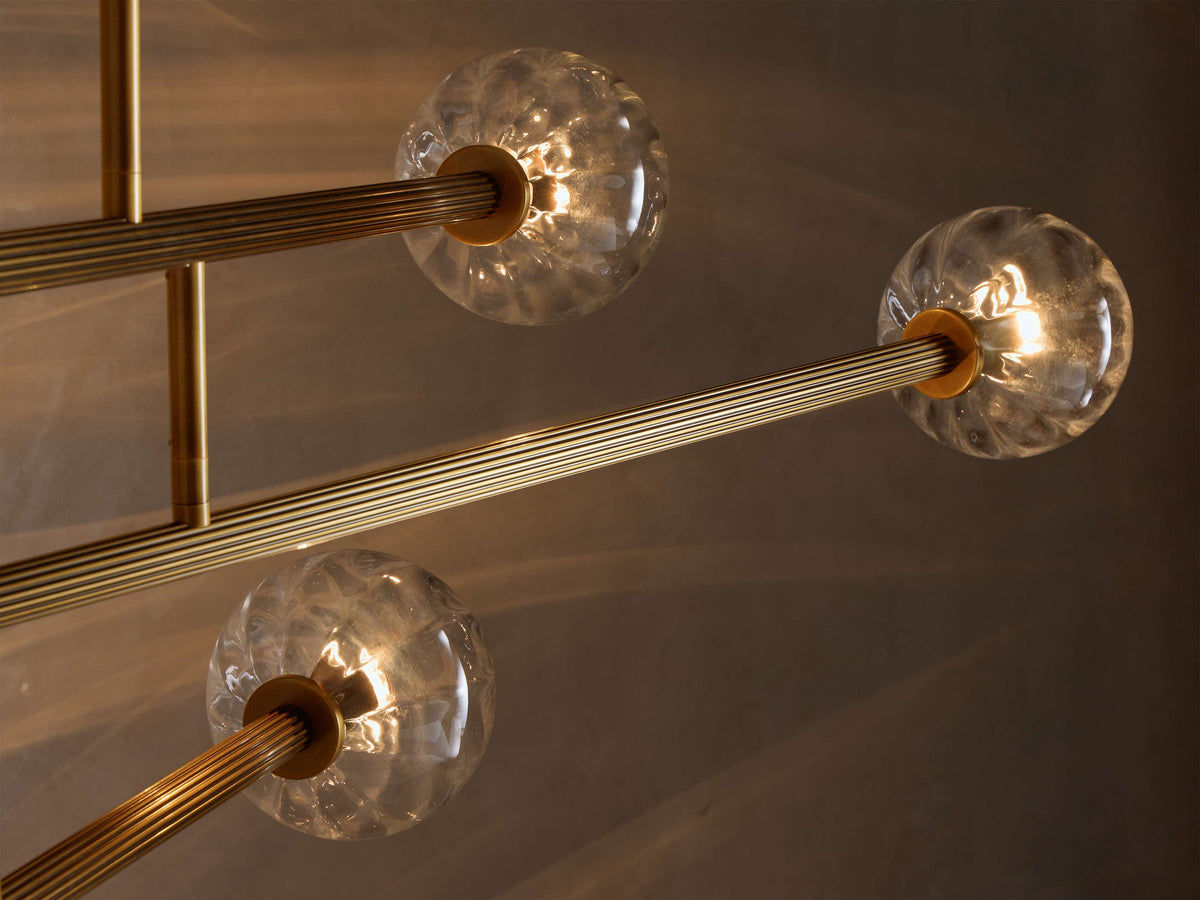 Close-up of an illuminated Brass and Glass Globe Chandelier‚Ñ¢ with clear, textured glass orbs and ribbed gold-toned arms.