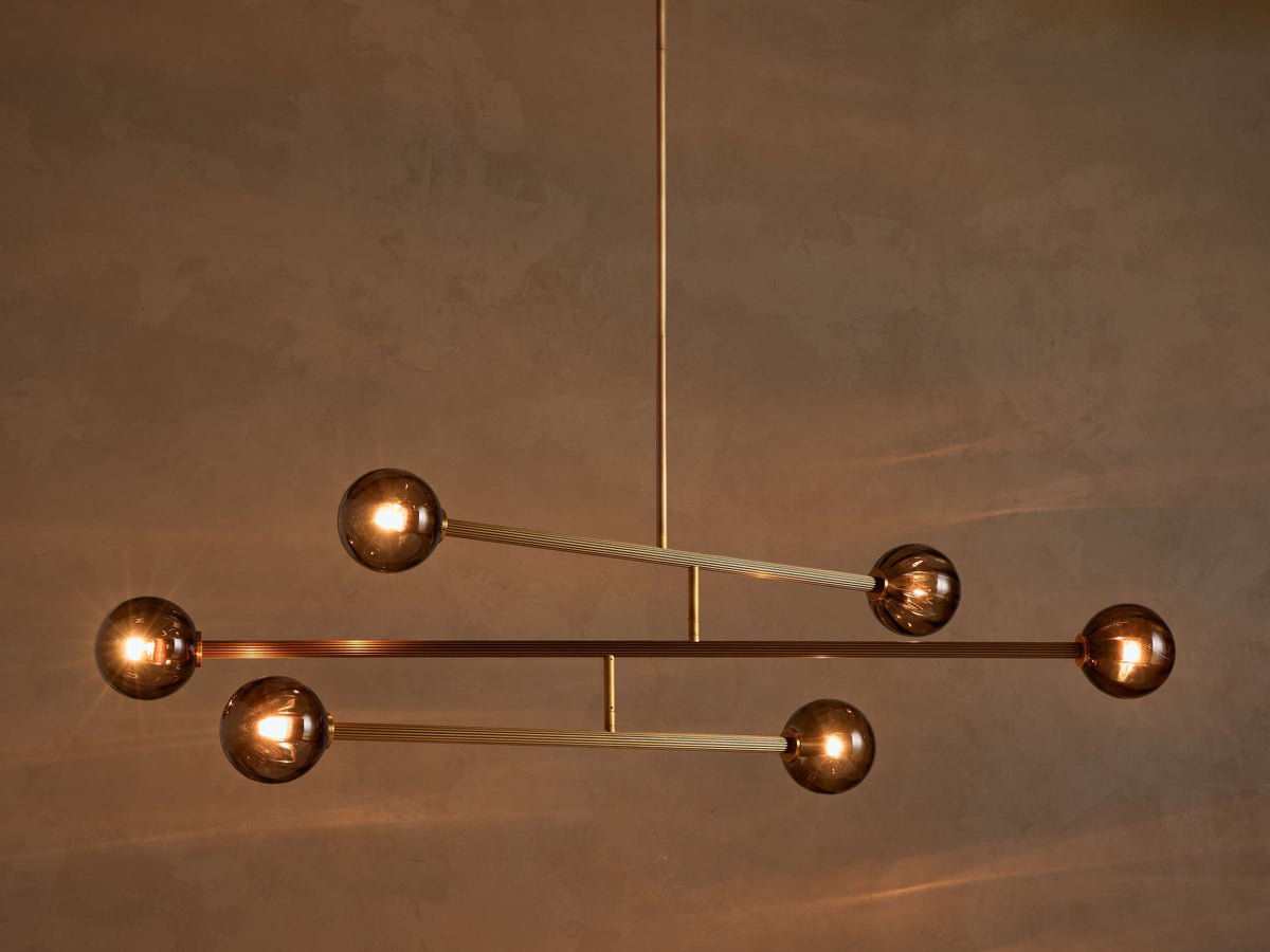 Modern chandelier with a vertical brass rod, horizontal ribbed brass arms, and six illuminated spherical smoky glass bulbs.