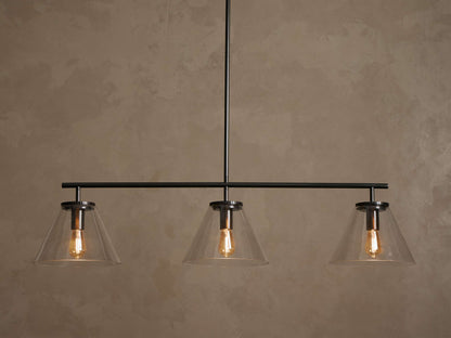 Front view of a black linear pendant light fixture with three clear conical glass shades and exposed warm Edison bulbs.