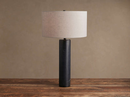 Brixton Table Lamp with a black marble cylindrical base and a light gray fabric drum shade, standing on a wooden surface.