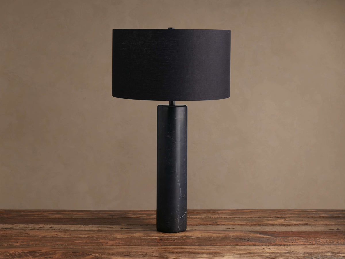 Close-up of Brixton Table Lamp's cylindrical dark gray marble base with white veining, featuring a black steel stem.