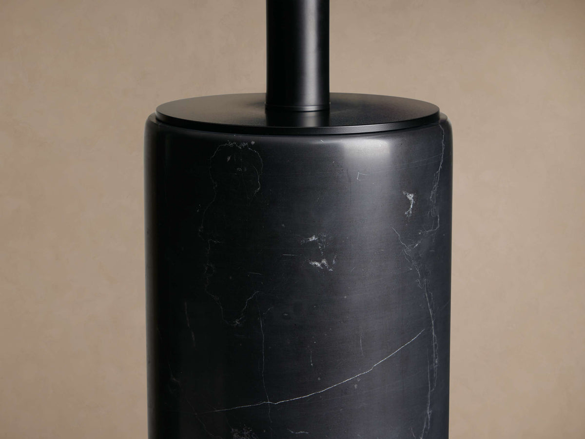 Brixton Table Lamp with a dark cylindrical marble base and a black fabric drum shade, standing on a rustic wooden table.