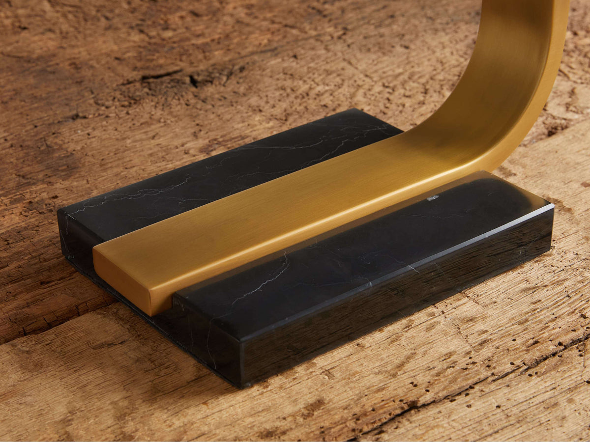 Close-up of Karson Task Table Lamp's black marble base with a brass-finished support, sitting on a rustic wooden surface.