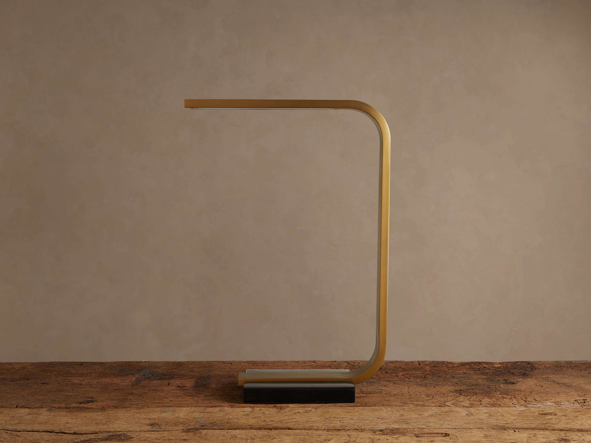 Karson Task Table Lamp, modern U-shaped design with brass finish and black marble base, on a rustic wood table.