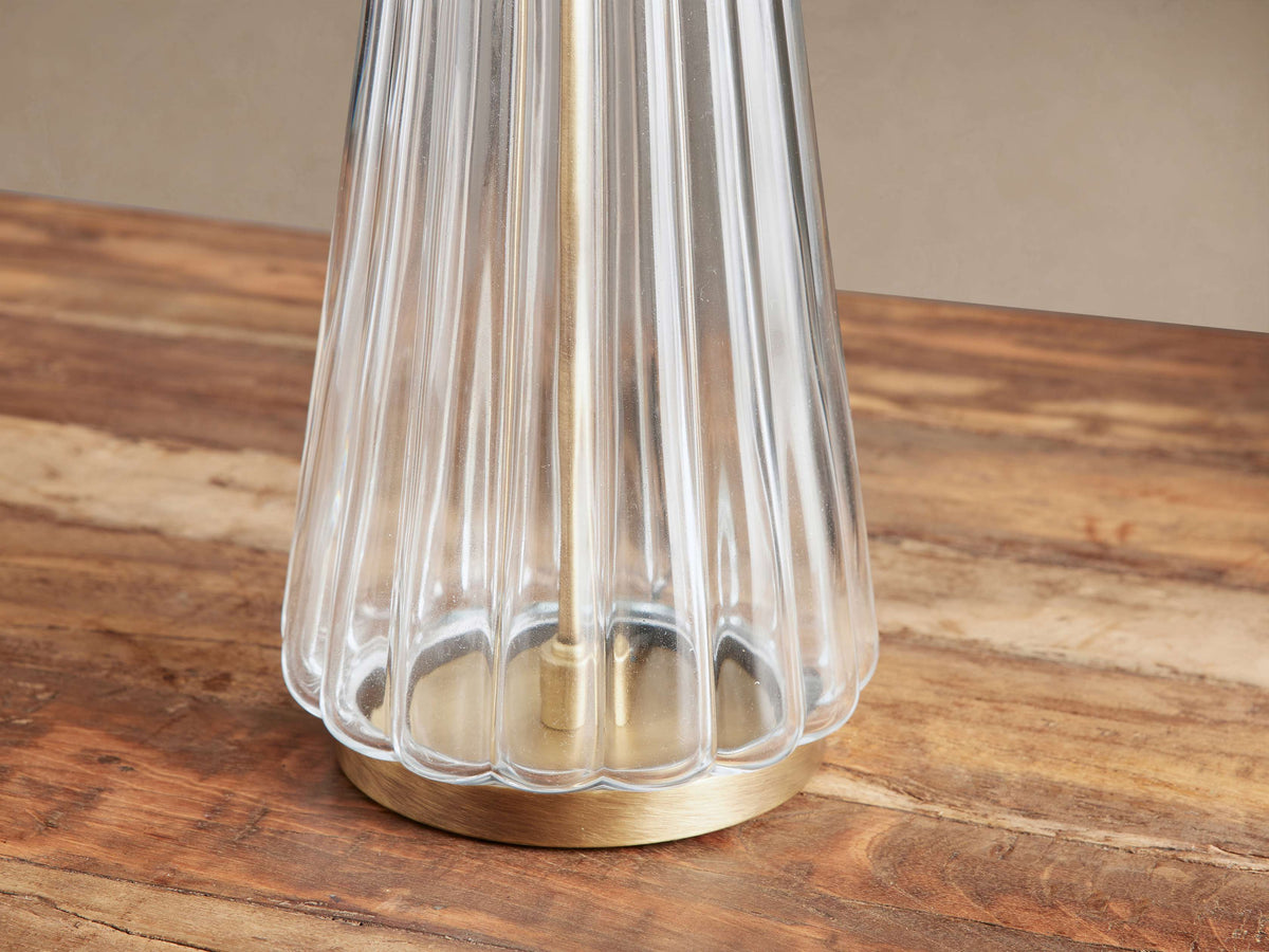 Close-up of Elisabetta Table Lamp with clear fluted glass, brass-finished round base, sitting on a warm brown wooden table.