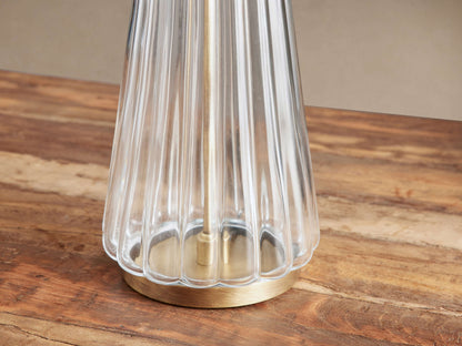 Close-up of Elisabetta Table Lamp with clear fluted glass, brass-finished round base, sitting on a warm brown wooden table.