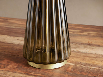 Elisabetta Table Lamp, close-up of its fluted smoky glass base and round brass-finished steel base on a wooden table.