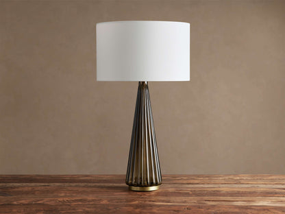 Elisabetta Table Lamp with a dark fluted glass conical base, brass-finish bottom, and white linen shade on a wood table.