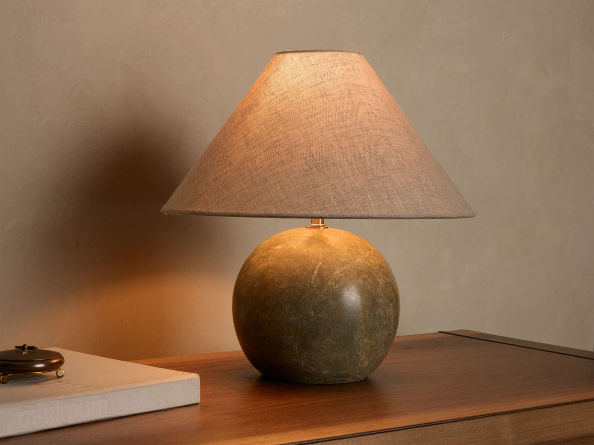 Front view of a table lamp with a round, mottled dark green stone base and an illuminated light brown conical fabric shade.