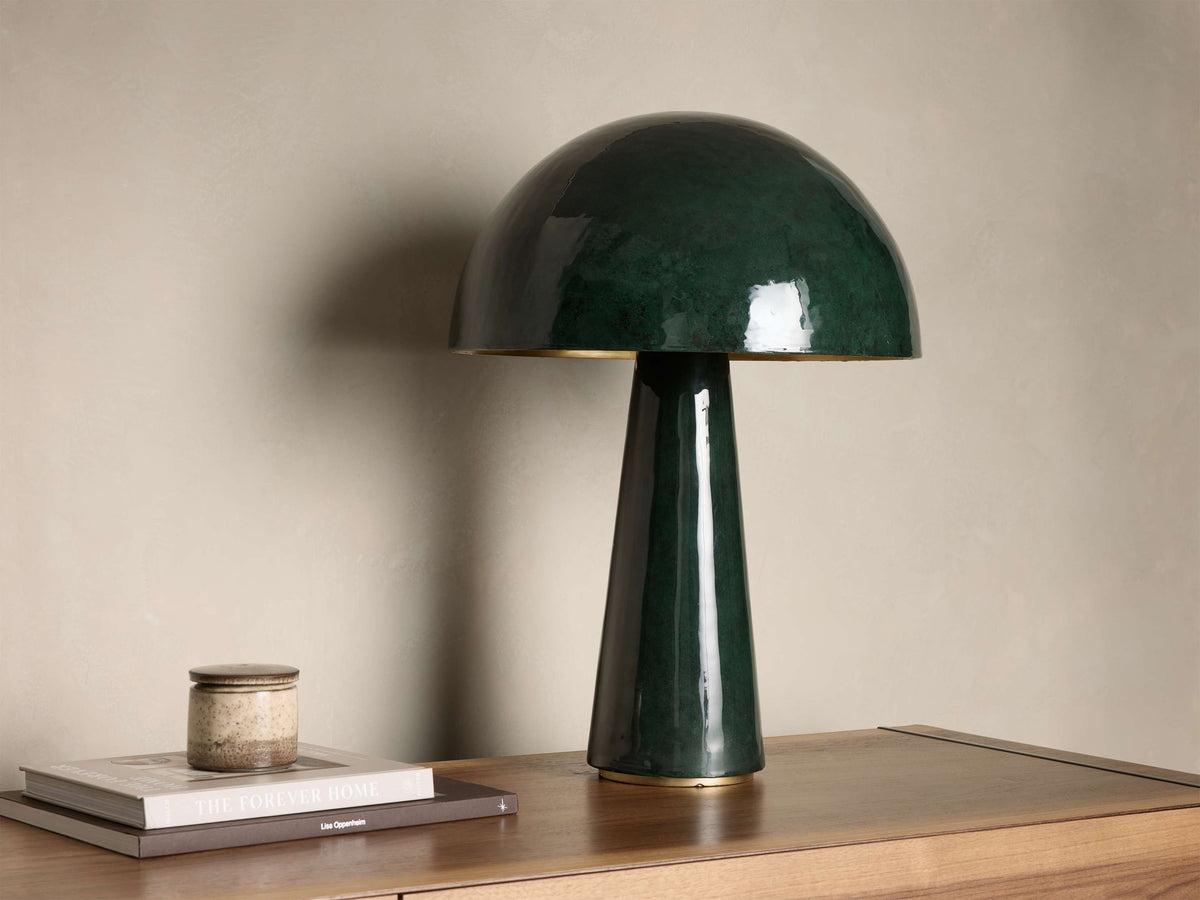 Glossy dark green mushroom-shaped table lamp with a gold base accent, placed on a wooden nightstand with books.