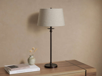 Front view of the Winslow Table Lamp with an antique bronze finish and light fabric shade on a wooden table.