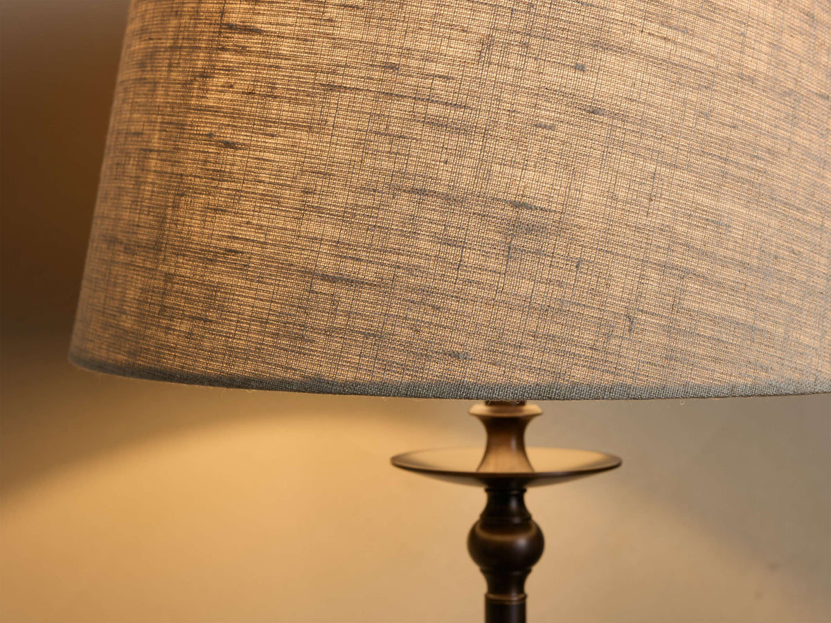 Close-up of the textured gray fabric shade and dark bronze-finished base of the Winslow Table Lamp, glowing with light.