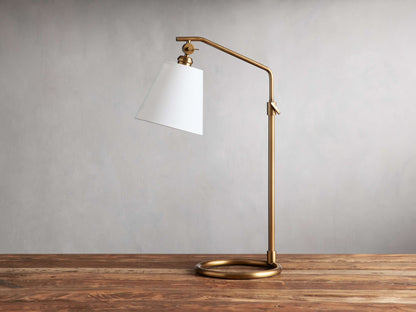 Kellen Table Lamp with an antiqued-brass frame, white linen shade, adjustable height on wooden table, simple design.