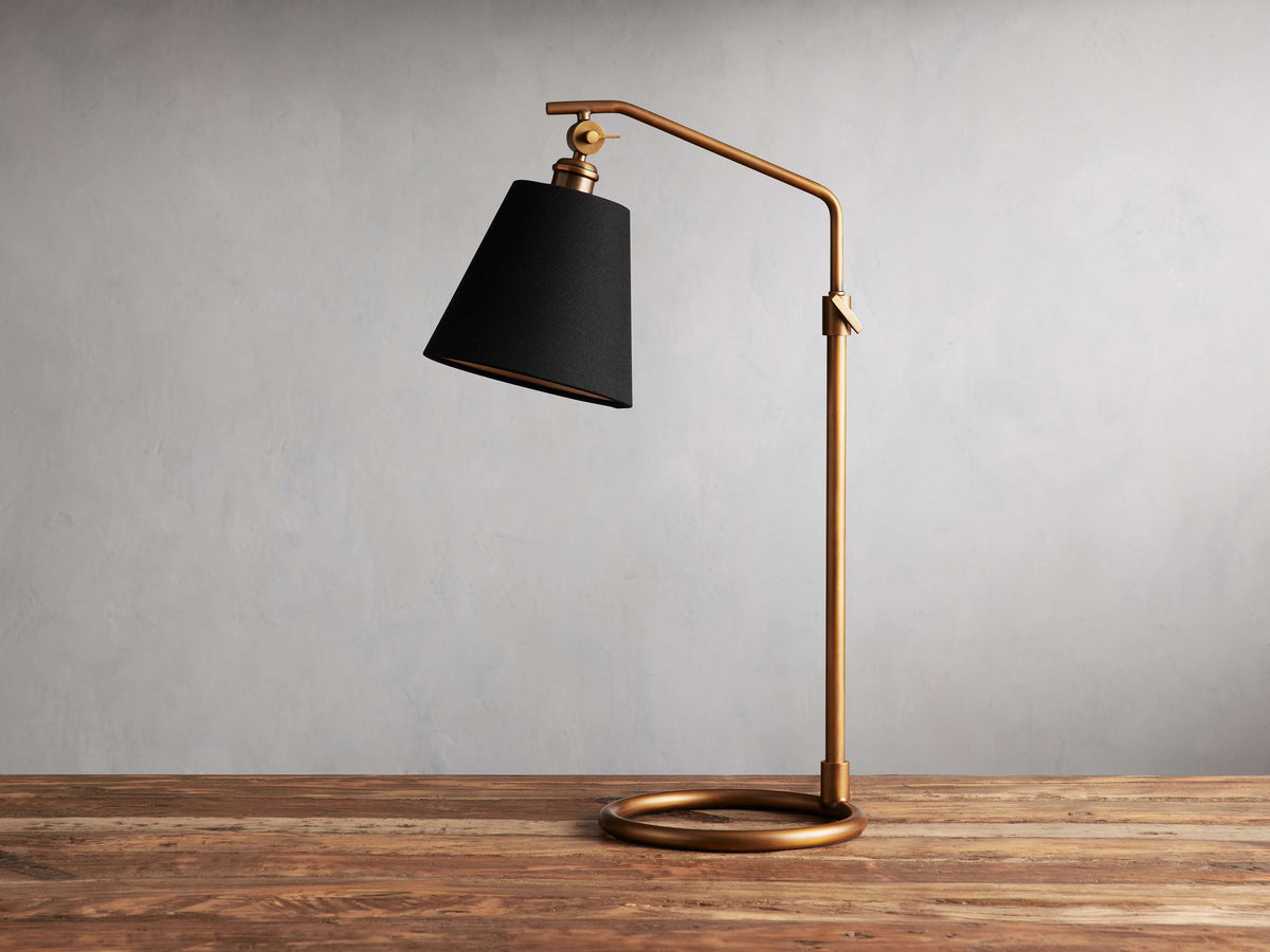 Kellen Antiqued Brass Table Lamp with adjustable height, black linen shade, and brass arm on a wooden surface.